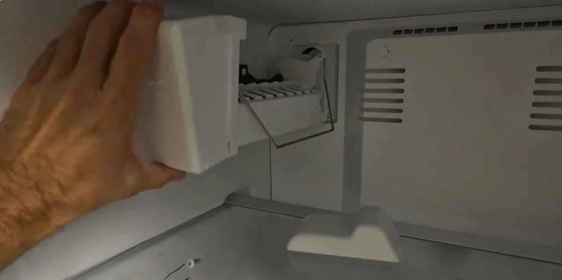 Technician repairing an ice maker inside a freezer compartment